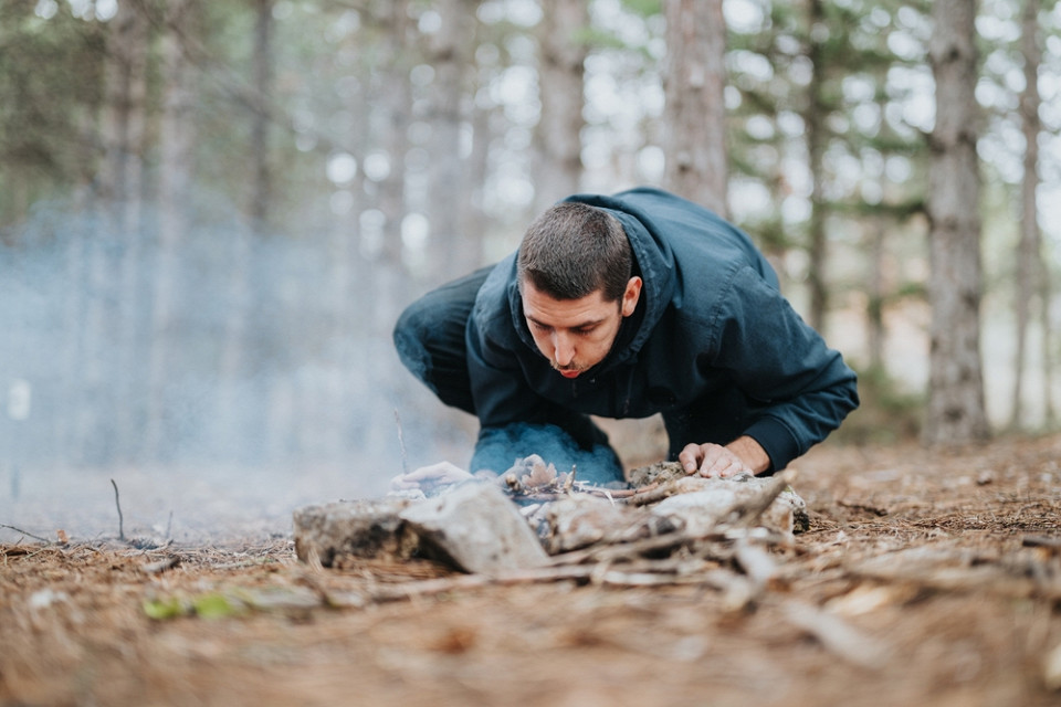 Мужчина разводит костер в лесу