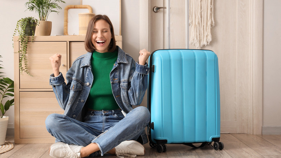 Счастливая девушка сидит на полу в квартире с чемоданом
